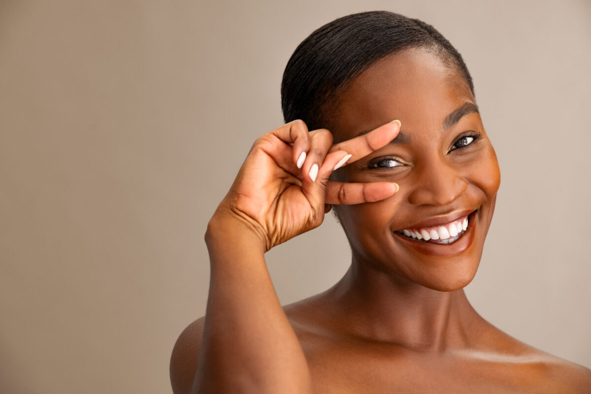 Femme souriante montrant la zone du contour des yeux, en lien avec le traitement des cernes par acide hyaluronique.
