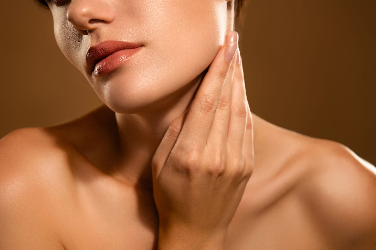 Femme touchant la zone de son menton et de l’ovale du visage, illustrant les zones souvent traitées par injections d’acide hyaluronique.