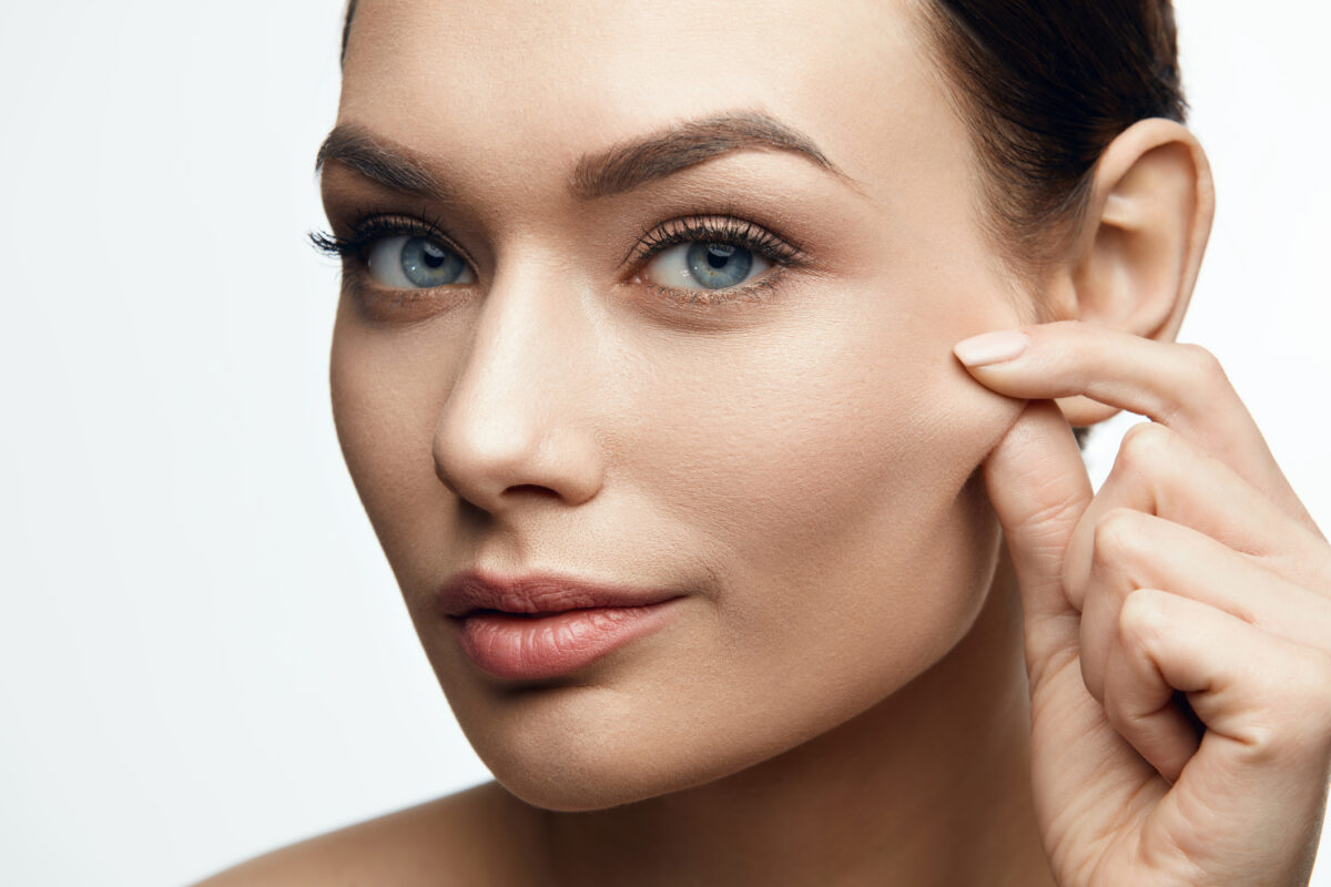 Femme montrant la peau de sa joue pour illustrer la perte de tonicité du visage.